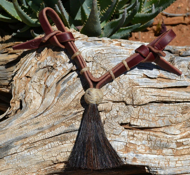 Jose Ortiz handmade 1/2" latigo leather curb strap with tightly braided natural rawhide knot and black mane horsehair tassel.  9" in length and attaches with self-tie bit attachments and no metal hardware. 