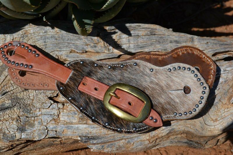 Close Up View Cowboy Style Hair-On Cowhide Shaped Spur Straps.  Hair-on cowhide with grey & brown brindle coloring with stainless steel spots.  Soft distressed leather lining and Hermann Oak harness leather straps.  Brass buckles.