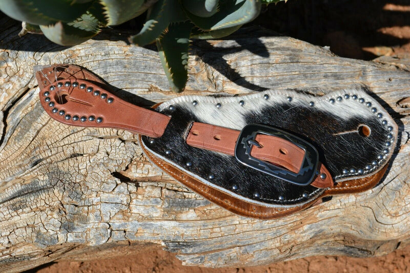 Close Up View Cowboy Style Hair-On Cowhide Shaped Spur Straps.  Hair-on cowhide with black & white coloring with stainless steel spots.  Soft distressed leather lining and Hermann Oak harness leather straps. 