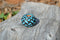 Close up View Hand braided rawhide scarf slide. Custom made in two-tone combinations of black and bright colored leather braided in a custom "checkerboard" pattern.   Turquoise/Black